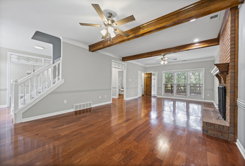 Unfurnished living room featuring crown molding, beamed ceiling, dark wood-type flooring, ceiling fan, and a brick fireplace