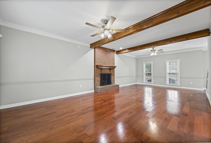 Unfurnished living room with beam ceiling, dark wood-style floors, crown molding, a fireplace, and ceiling fan