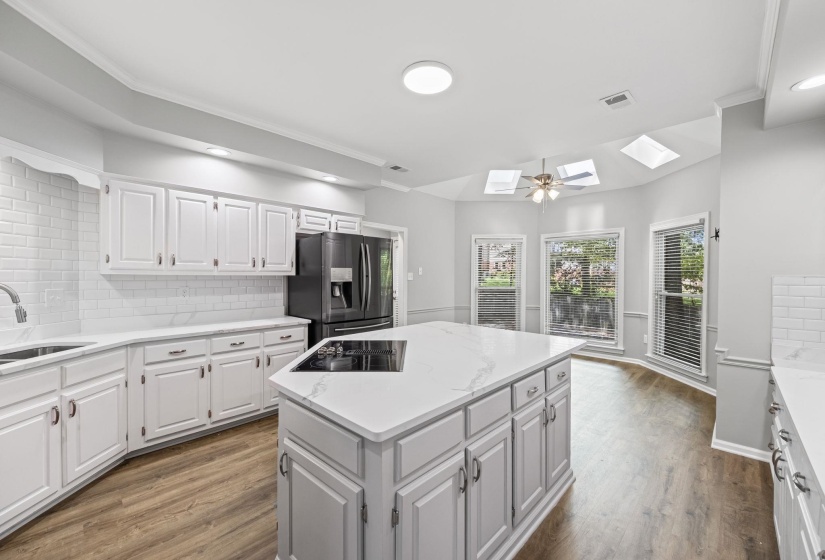 Kitchen with tasteful backsplash, a skylight, white cabinets, dark wood-type flooring, and recessed lighting