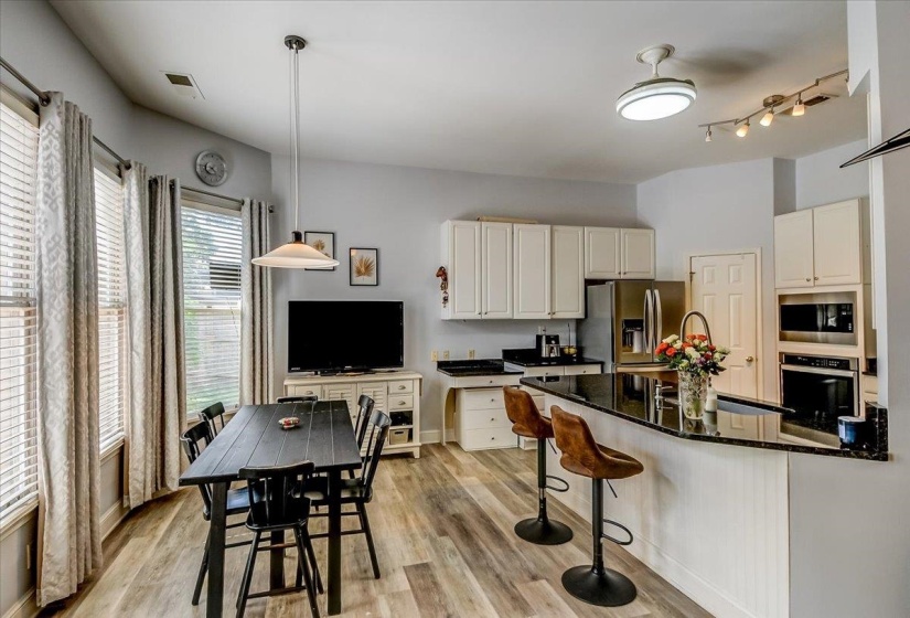 Open-concept kitchen and dining area featuring wood-finish flooring, white cabinetry, dark countertops, and stainless steel appliances