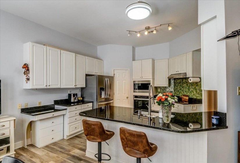 Kitchen featuring white cabinetry, dark speckled countertops, stainless steel appliances, a green mosaic tile backsplash, and wood-finish flooring