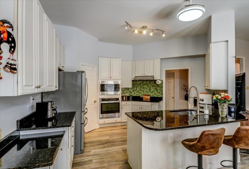 Kitchen featuring white cabinetry, dark speckled countertops, stainless steel appliances, and wood-finish flooring