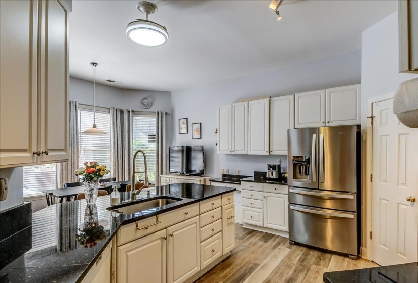 Expansive kitchen featuring a large island with an integrated sink, ample white cabinetry, dark countertops, a stainless steel refrigerator, and wood-finish flooring