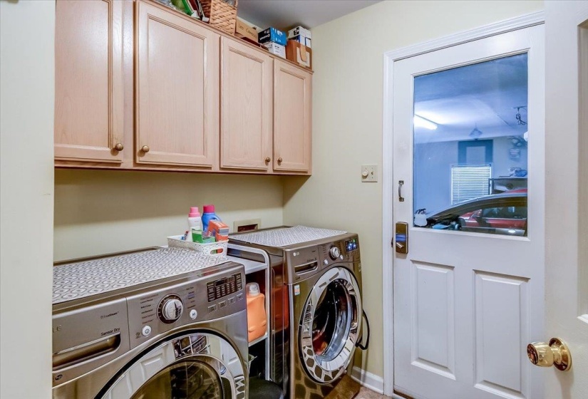 Laundry area with light wood-finish cabinetry, neutral wall paint, and a white door with a clear glass upper panel
