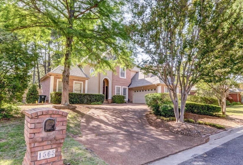 Traditional brick and stucco exterior residence featuring a two-car garage, mature trees, and a brick mailbox