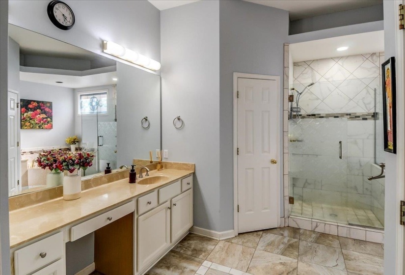 Bathroom featuring a dual vanity with a light-toned countertop, a large framed mirror, and a spacious walk-in shower with glass enclosure