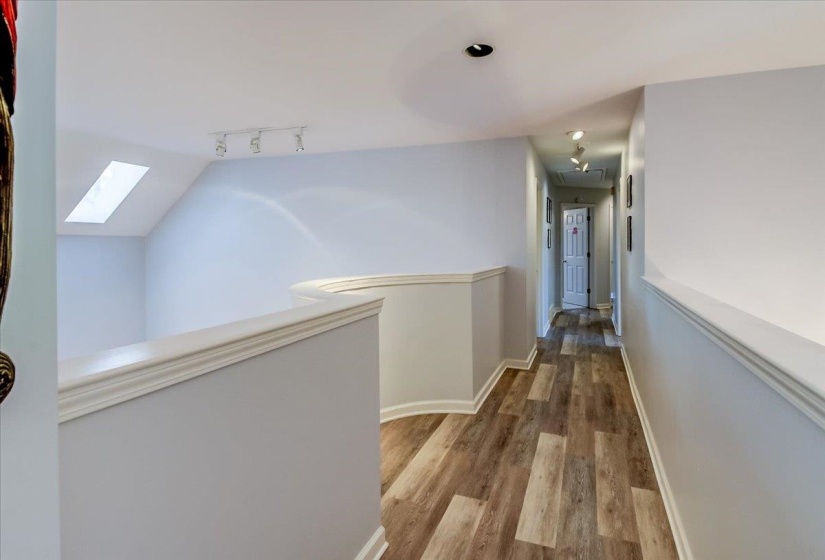 Upper-level hallway featuring wood-finish flooring, recessed lighting, a skylight, track lighting, and a white paneled door