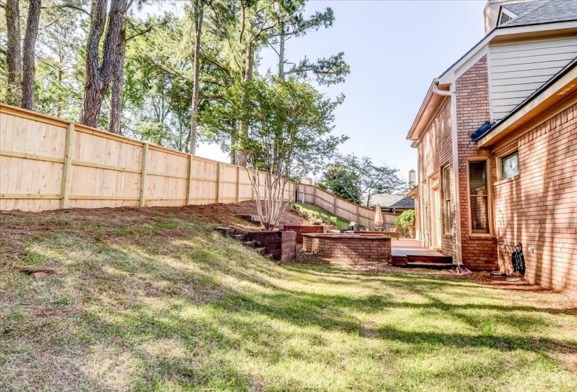 Expansive backyard featuring a newly installed privacy fence, a multi-level deck, and brick retaining walls