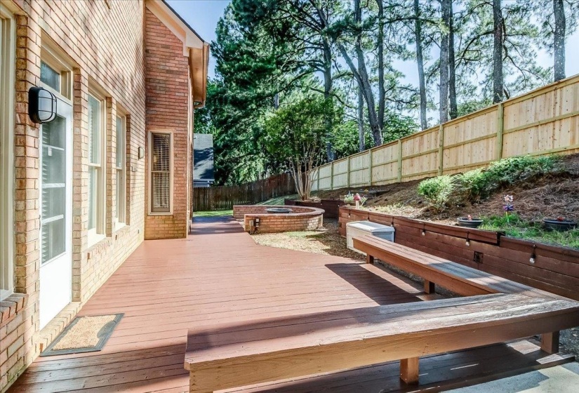 Expansive wood-finish deck with built-in seating, featuring a brick exterior, a new wood privacy fence, and tiered landscaping