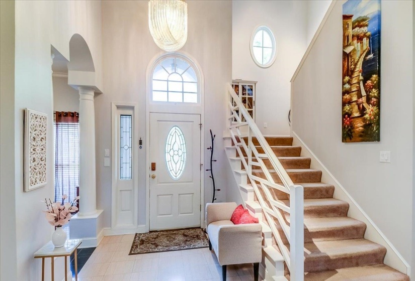 Two-story foyer with a vaulted ceiling, a chandelier, and light wood-finish flooring