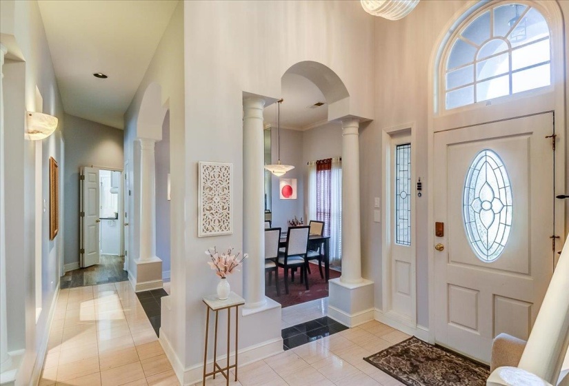 Entryway featuring a decorative leaded glass front door with an arched transom window, ceramic tile flooring, and architectural columns framing an arched opening