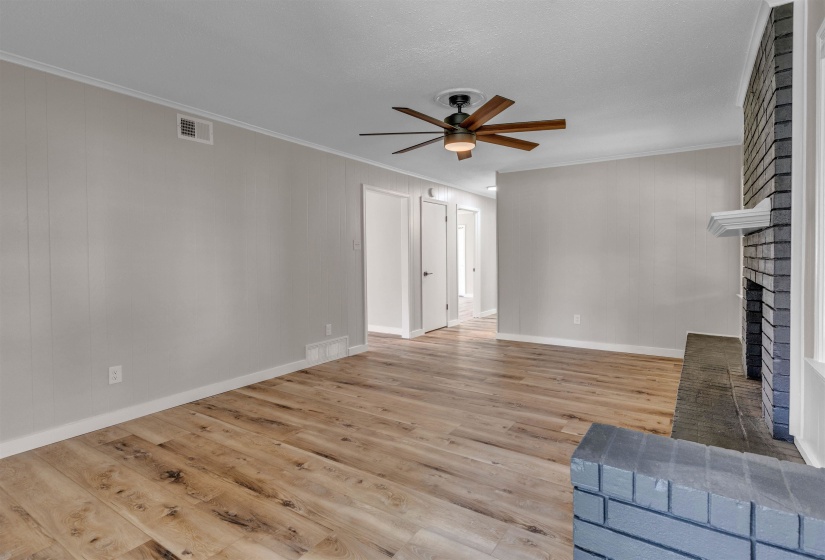 Living area featuring wood-finish flooring, light gray walls with vertical paneling, and a dark brick fireplace with a white mantel