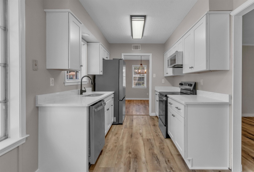 Galley kitchen featuring white cabinetry, light-toned countertops, and wood-finish flooring