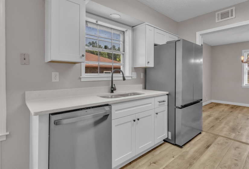 Kitchen featuring white cabinetry, light-toned countertops, a stainless steel dishwasher, a stainless steel refrigerator, and wood-finish flooring