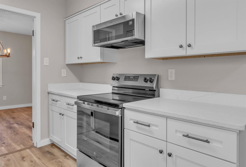 Kitchen featuring white shaker-style cabinetry, stainless steel appliances, solid surface countertops, and wood-finish flooring