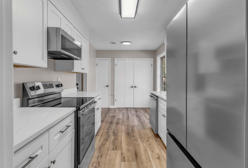 Galley kitchen featuring white cabinetry, light-toned countertops, and wood-finish flooring