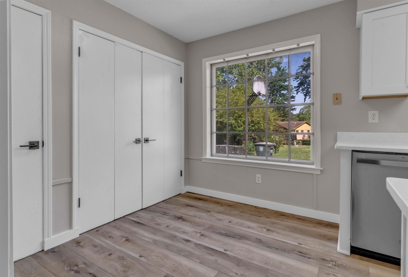 Interior featuring wood-finish flooring, two white doors with dark hardware, a large grid-pattern window, and a white countertop with an under-counter appliance