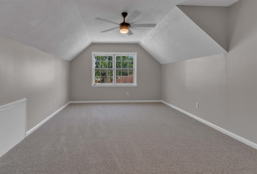 Carpeted room featuring sloped ceilings, a centered window, and a ceiling fan with integrated lighting