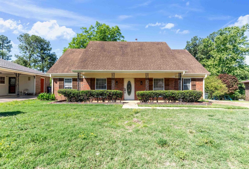 Brick facade with a covered front porch, featuring decorative metal columns and a white oval-light entry door