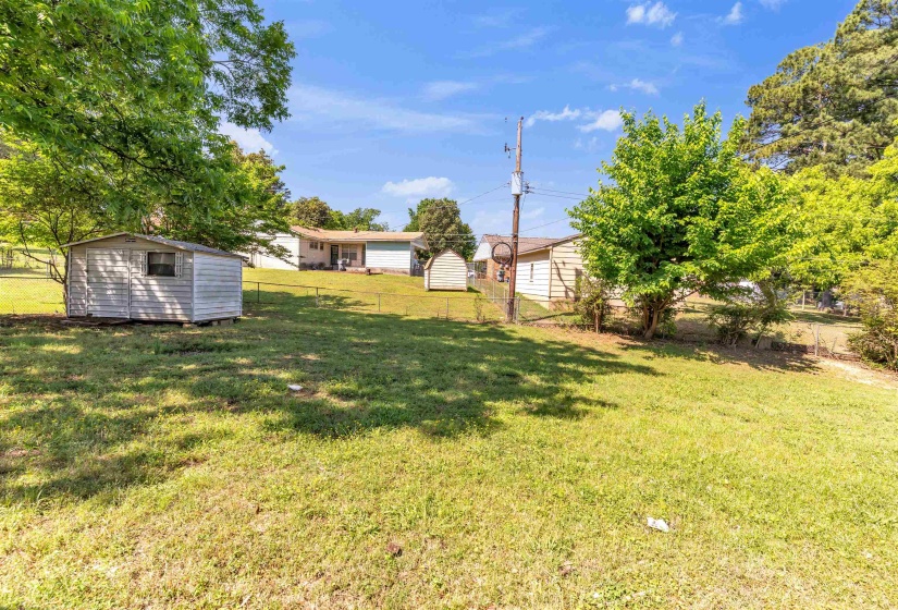 Expansive backyard with a storage shed, mature trees, and chain-link fencing