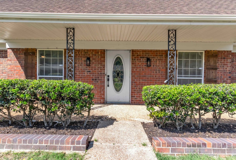 Brick facade entry with decorative wrought iron columns, an oval glass-paneled front door, and exterior lighting fixtures