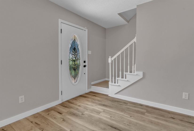 Entryway featuring a white door with an oval stained-glass insert, wood-finish flooring, light gray walls, white baseboards, and a white staircase with balusters