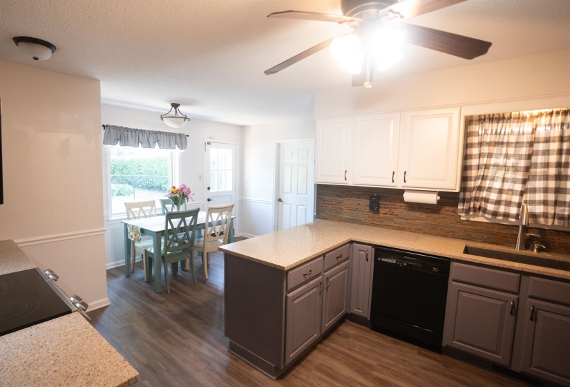 Bright kitchen featuring light-toned countertops, two-tone cabinetry with white upper and gray lower cabinets, a black dishwasher, and wood-finish flooring