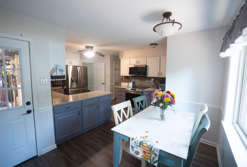 Kitchen area featuring wood-finish flooring, white cabinetry, stainless steel appliances, and a central island with a light-colored countertop