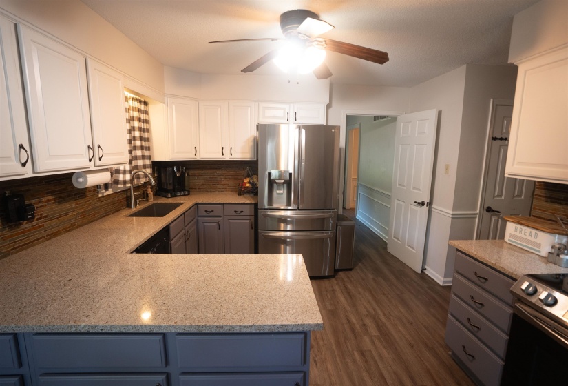 U-shaped kitchen featuring stone-finish countertops, two-tone cabinetry with upper white and lower gray finishes, a mosaic tile backsplash, and wood-look flooring