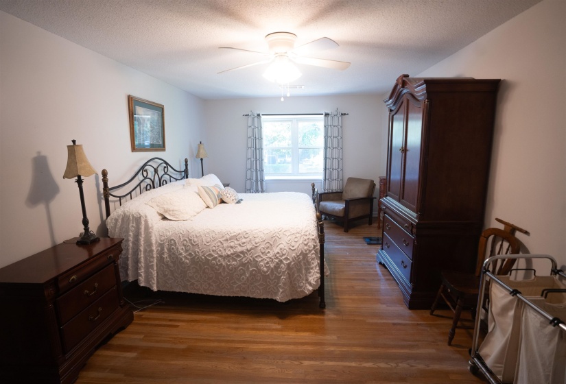 Spacious room featuring wood-finish flooring, a ceiling fan, and ample natural light from a window with patterned curtains