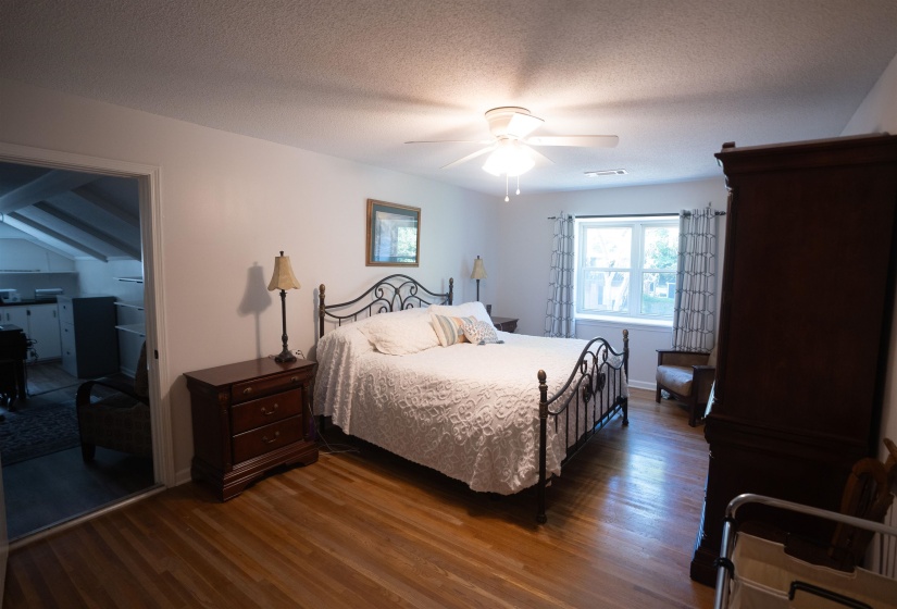 Spacious bedroom featuring wood-finish flooring, a ceiling fan with integrated lighting, and a window with natural light