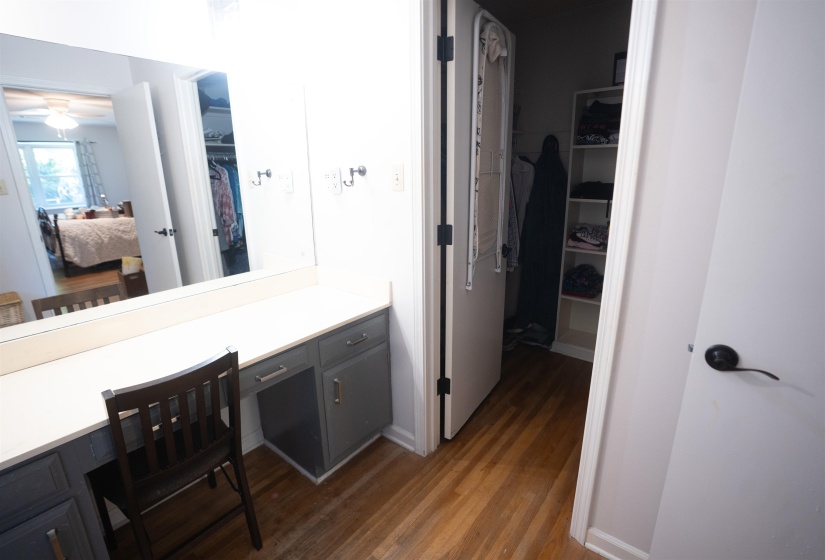 Vanity area featuring a built-in countertop with integrated mirror and shaker-style cabinetry, wood-finish flooring, and a walk-in closet with shelving