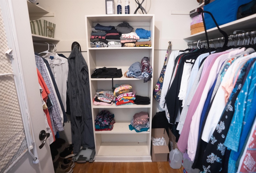 Walk-in closet featuring built-in shelving, multiple hanging rods, and wood-finish flooring