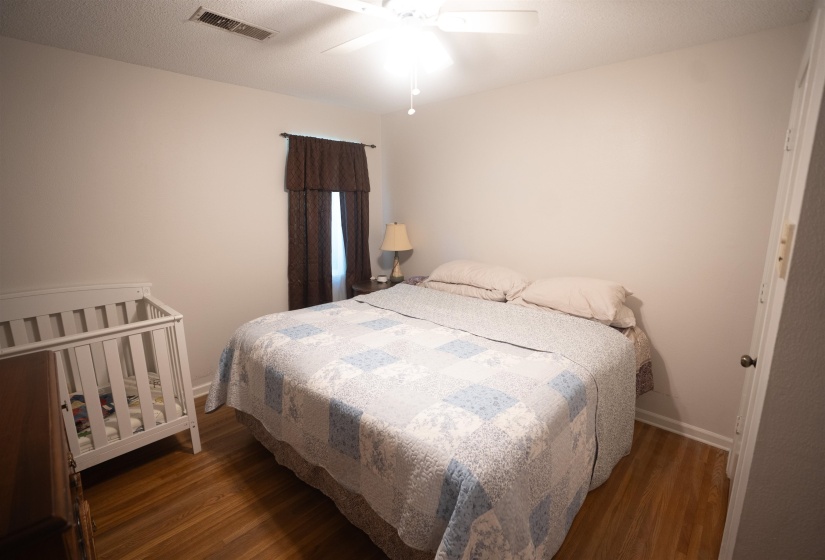 Bedroom featuring wood-finish flooring, a ceiling fan with integrated lighting, and a window with dark patterned drapes