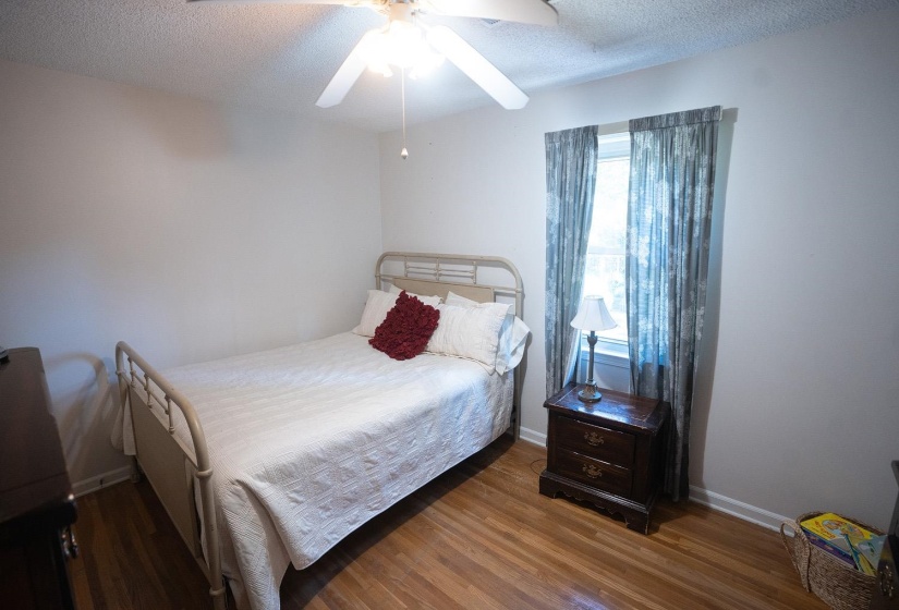 Room featuring wood-finish flooring, a ceiling fan with light fixture, and a window with curtains