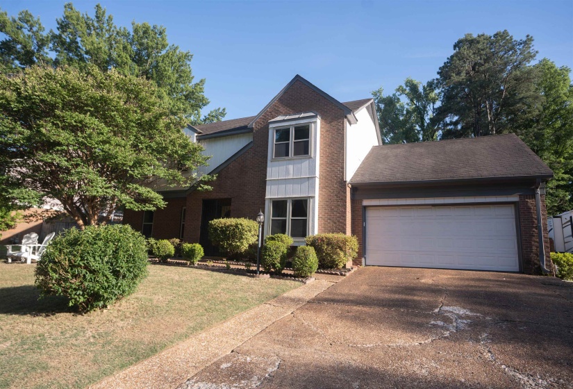 Brick and white siding exterior with a dark shingle roof, featuring a two-car garage, mature trees, and established landscaping