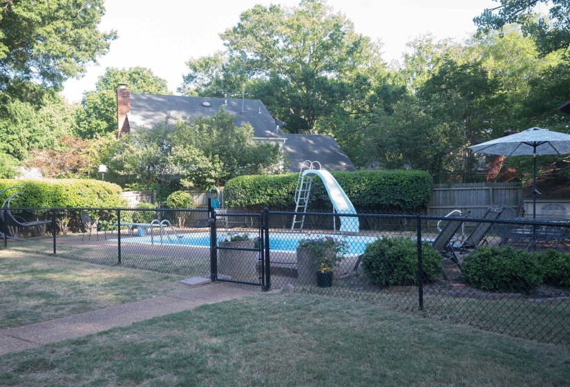 Private fenced-in swimming pool featuring a water slide, surrounding patio space, and mature perimeter landscaping
