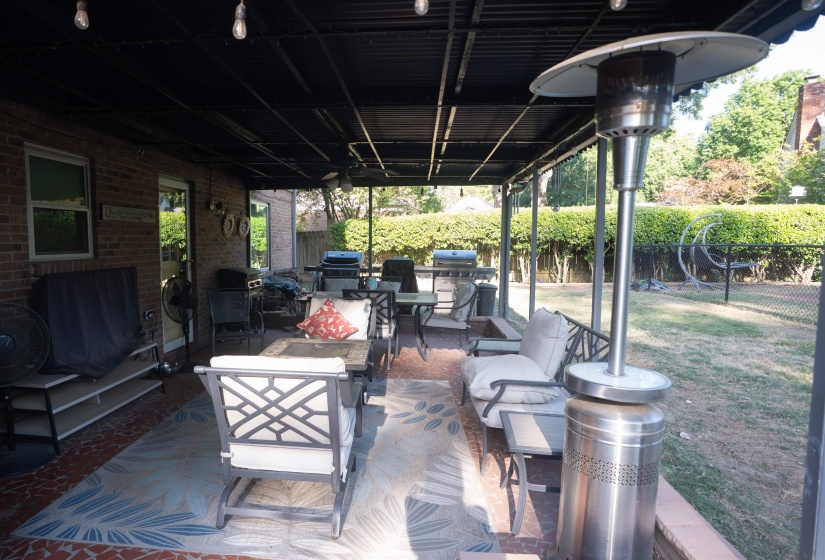 Covered patio featuring a brick exterior wall, black overhead structure, and string lighting