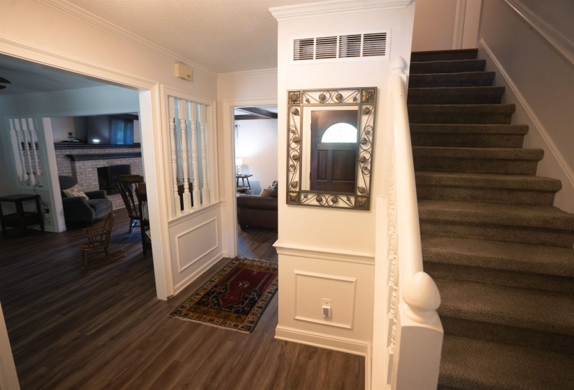 Entryway featuring wood-finish flooring, white wainscoting, and a carpeted staircase with a white banister