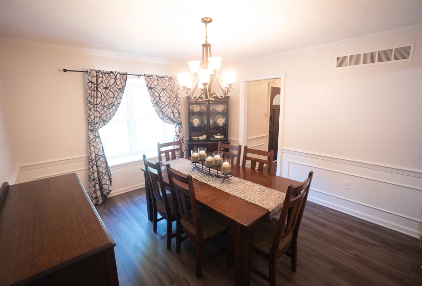 Formal dining space featuring wood-finish flooring, white wainscoting, and crown molding