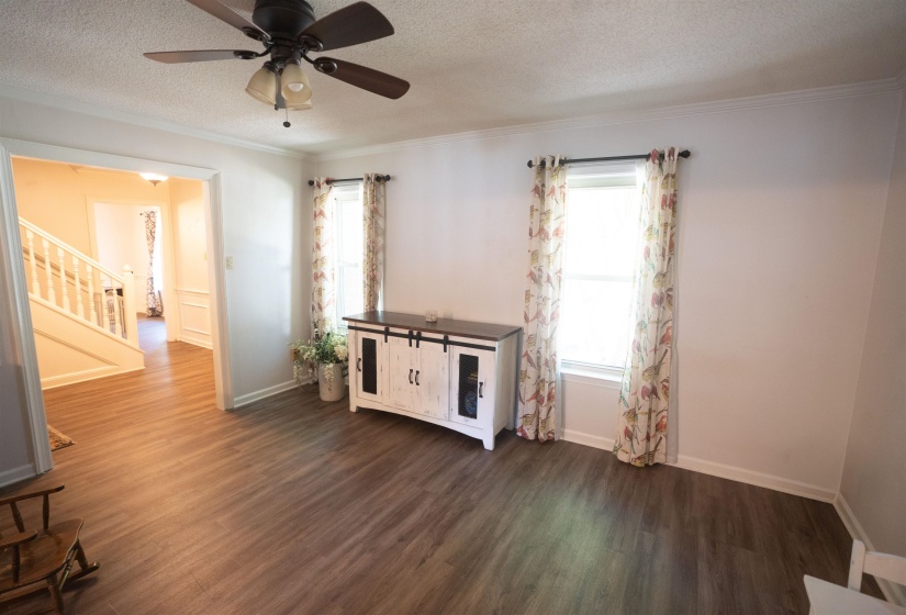 Wood-finish flooring throughout, featuring a ceiling fan with light fixture, crown molding, and white baseboards