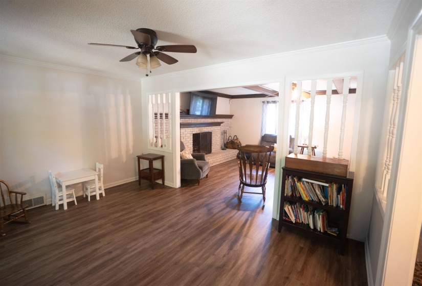 Open-concept living area featuring wood-finish flooring, a ceiling fan with integrated lighting, and crown molding