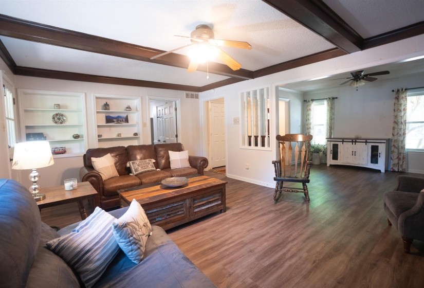 Spacious living area featuring wood-finish flooring, exposed ceiling beams, built-in shelving, and ceiling fans
