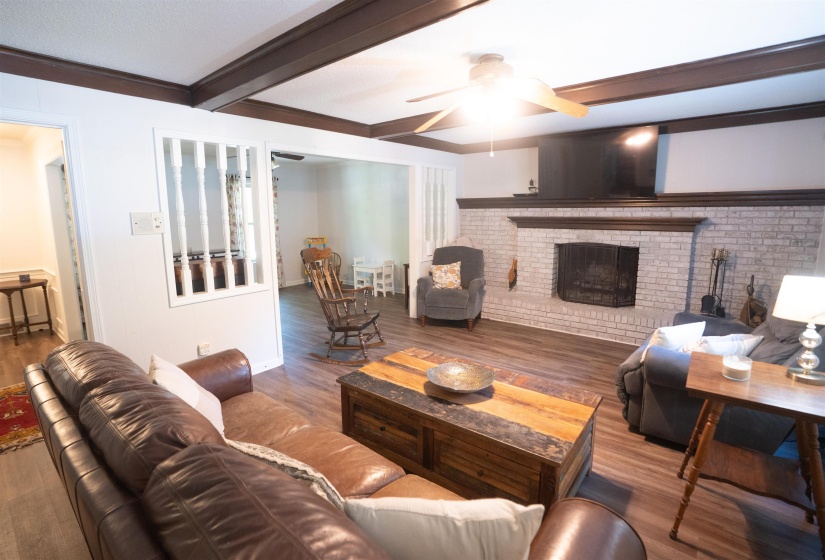 Living area featuring wood-finish flooring, a white-painted brick fireplace with a dark wood mantel, and a ceiling fan