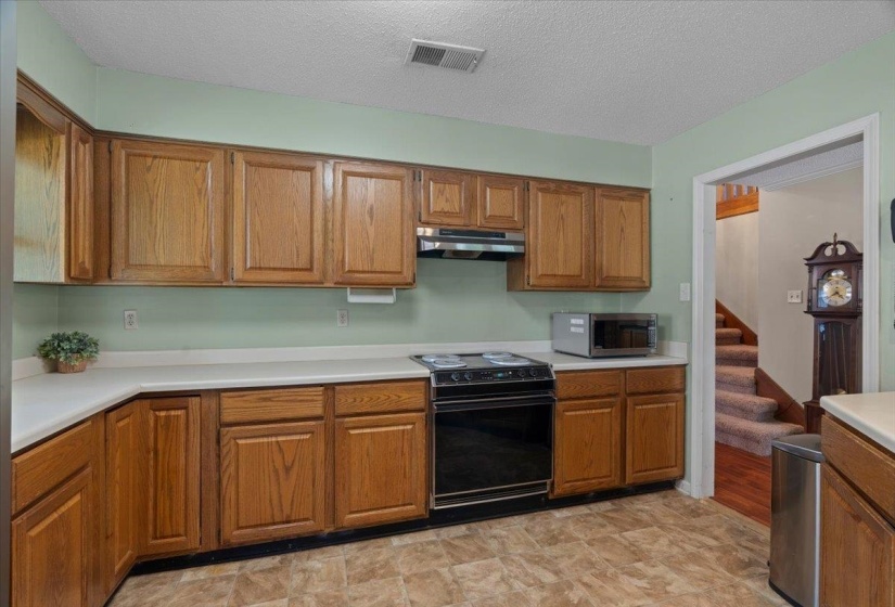 Kitchen featuring wood cabinetry, white countertops, black electric range, and wood-finish flooring