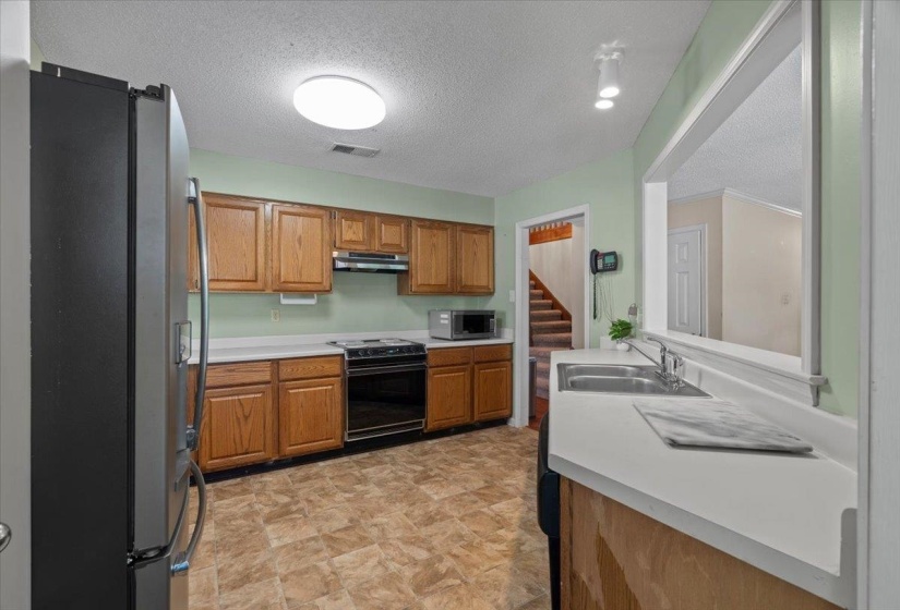 Kitchen featuring wood cabinetry, white countertops, a double basin stainless steel sink, black range, and sheet vinyl flooring