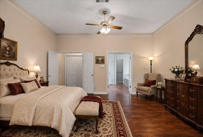 Spacious bedroom featuring wood-finish flooring, light-colored walls, crown molding, a ceiling fan, and double bi-fold closet doors