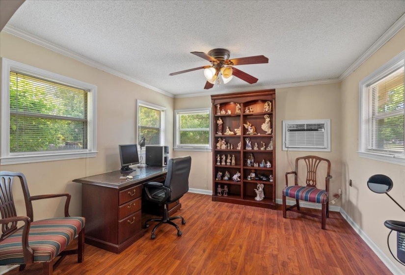 Spacious room featuring wood-finish flooring, multiple windows with blinds, a built-in wooden bookcase, and a ceiling fan with integrated lighting