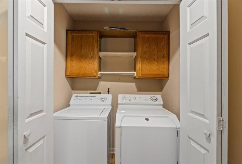 Dedicated laundry closet featuring bi-fold panel doors, two upper wood-finish cabinets, and two open shelves