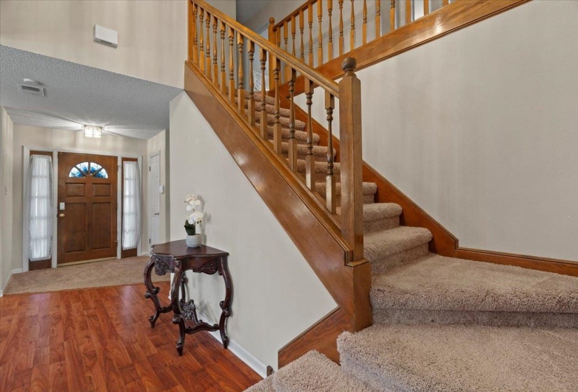 Foyer featuring wood-finish flooring, a wood-paneled front door with sidelights, and a two-story ceiling
